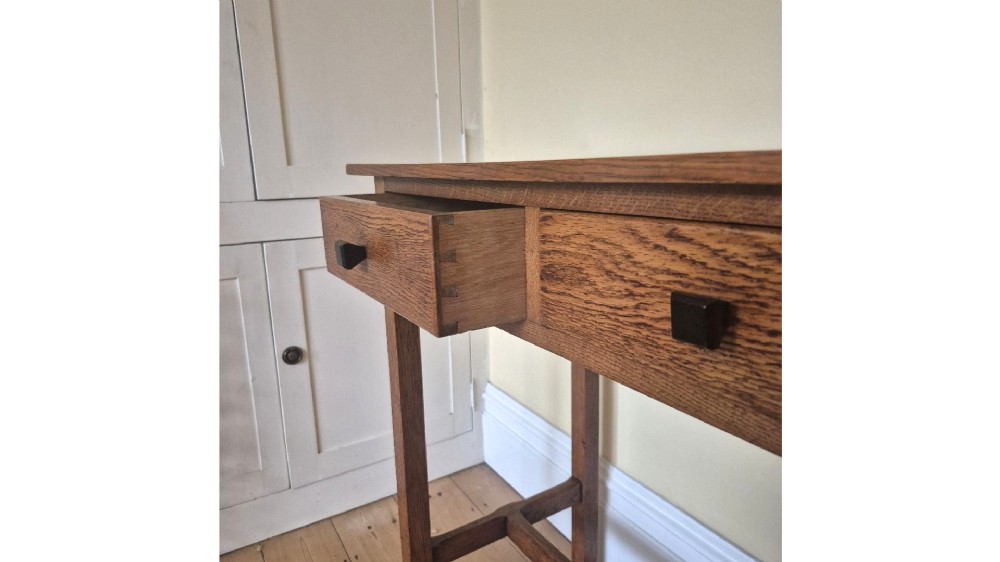 A medium brown antique oak side table featuring two drawers with dark square knobs, straight square legs, and an H-stretcher base. View X