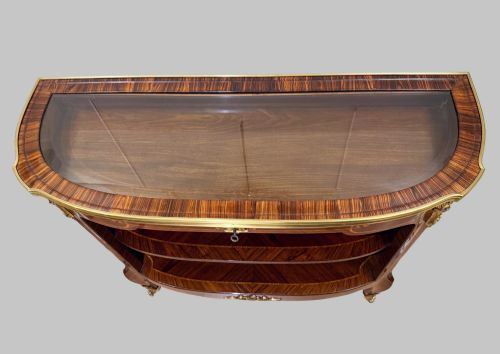 fig 1. A late 19th-century French Louis XV style demilune open bookcase featuring marquetry wood veneer, gilt-bronze ormolu mounts, open shelving, and a glass vitrine top.