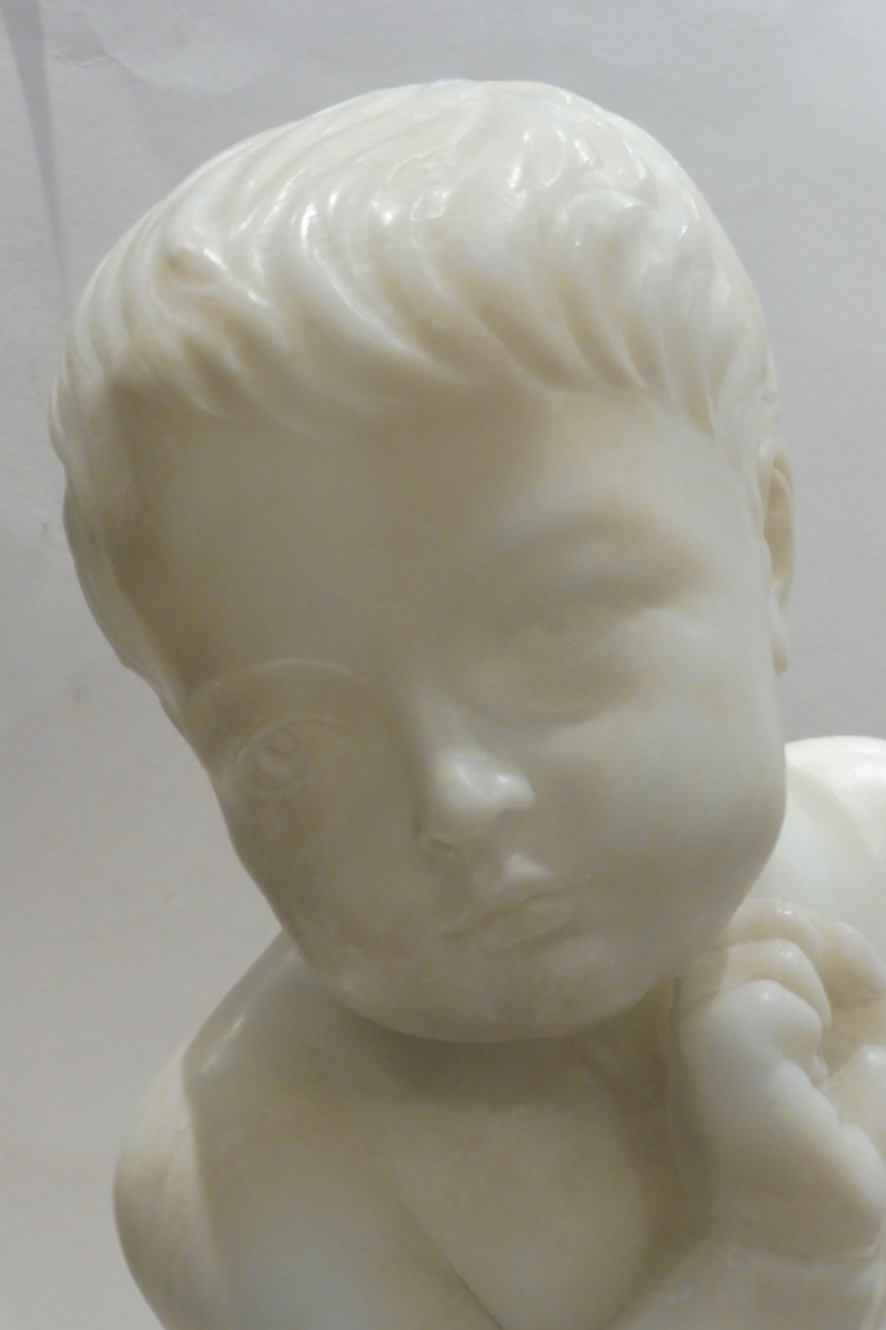 An Italian carved alabaster sculpture depicting a young seated boy beside a miniature birdcage, set on a grey veined marble base. View II