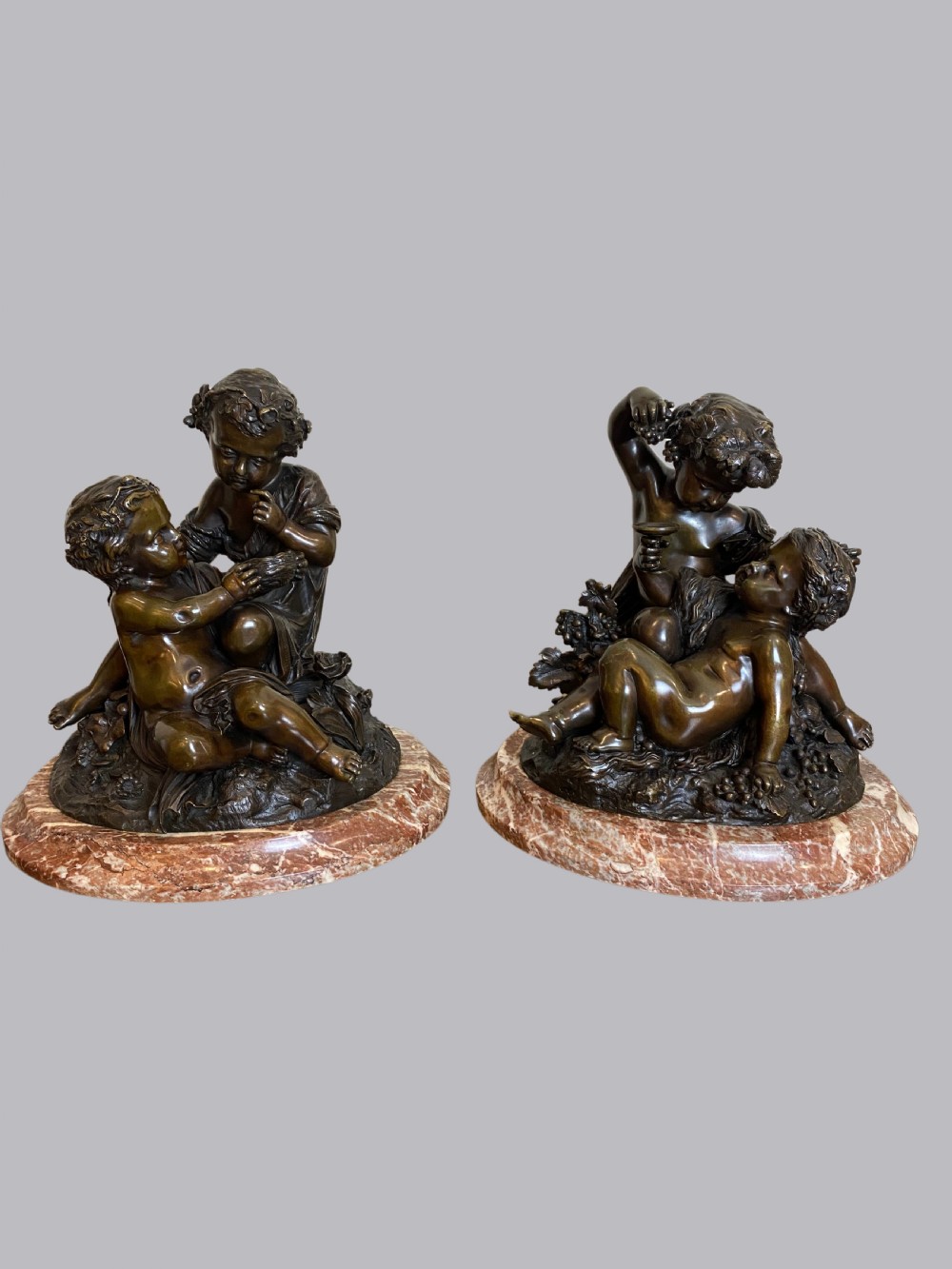 A pair of late 19th-century dark bronze sculptures depicting classical putti mounted on oval reddish veined marble bases.