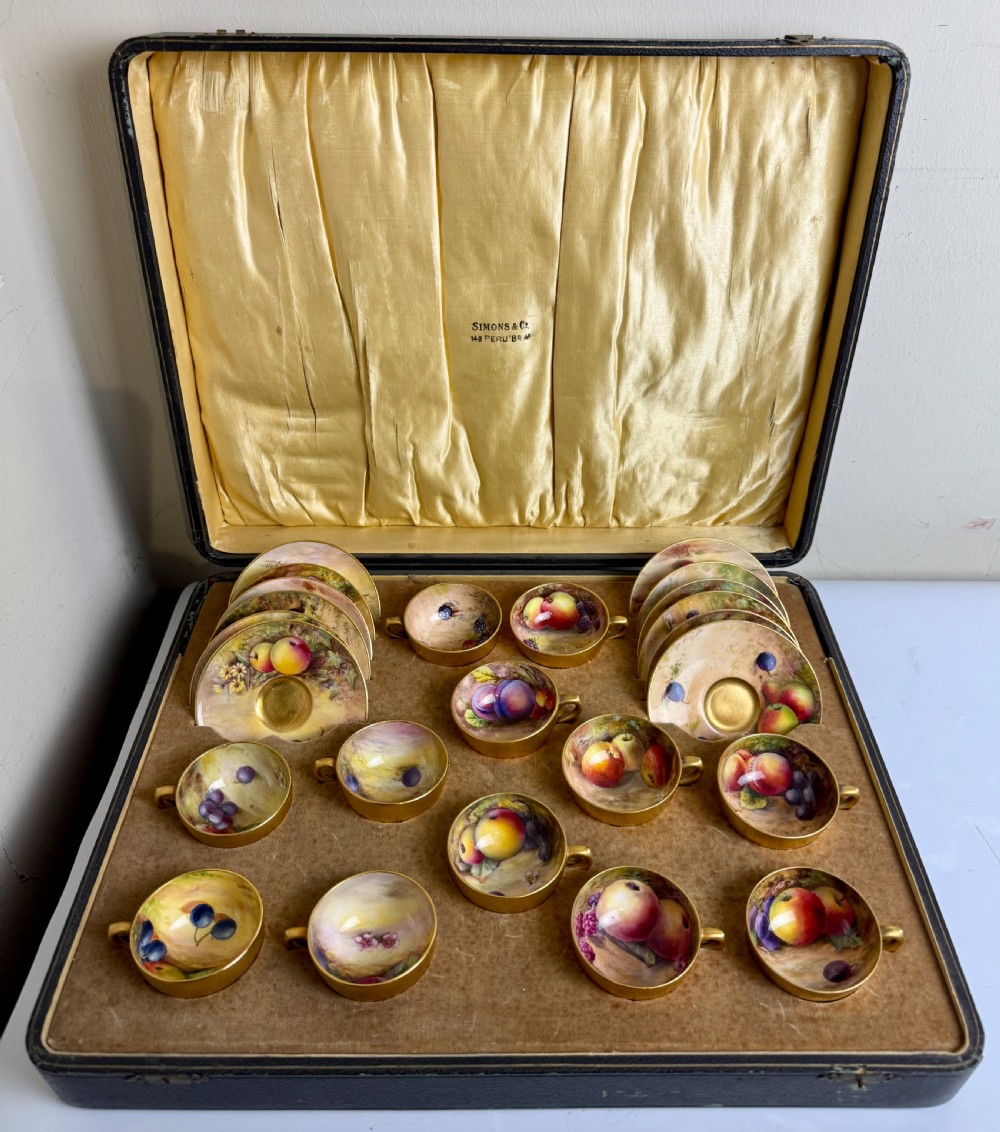 An open fitted presentation case containing twelve hand-painted porcelain demitasse coffee cups and saucers decorated with fruit motifs and gilded interiors.