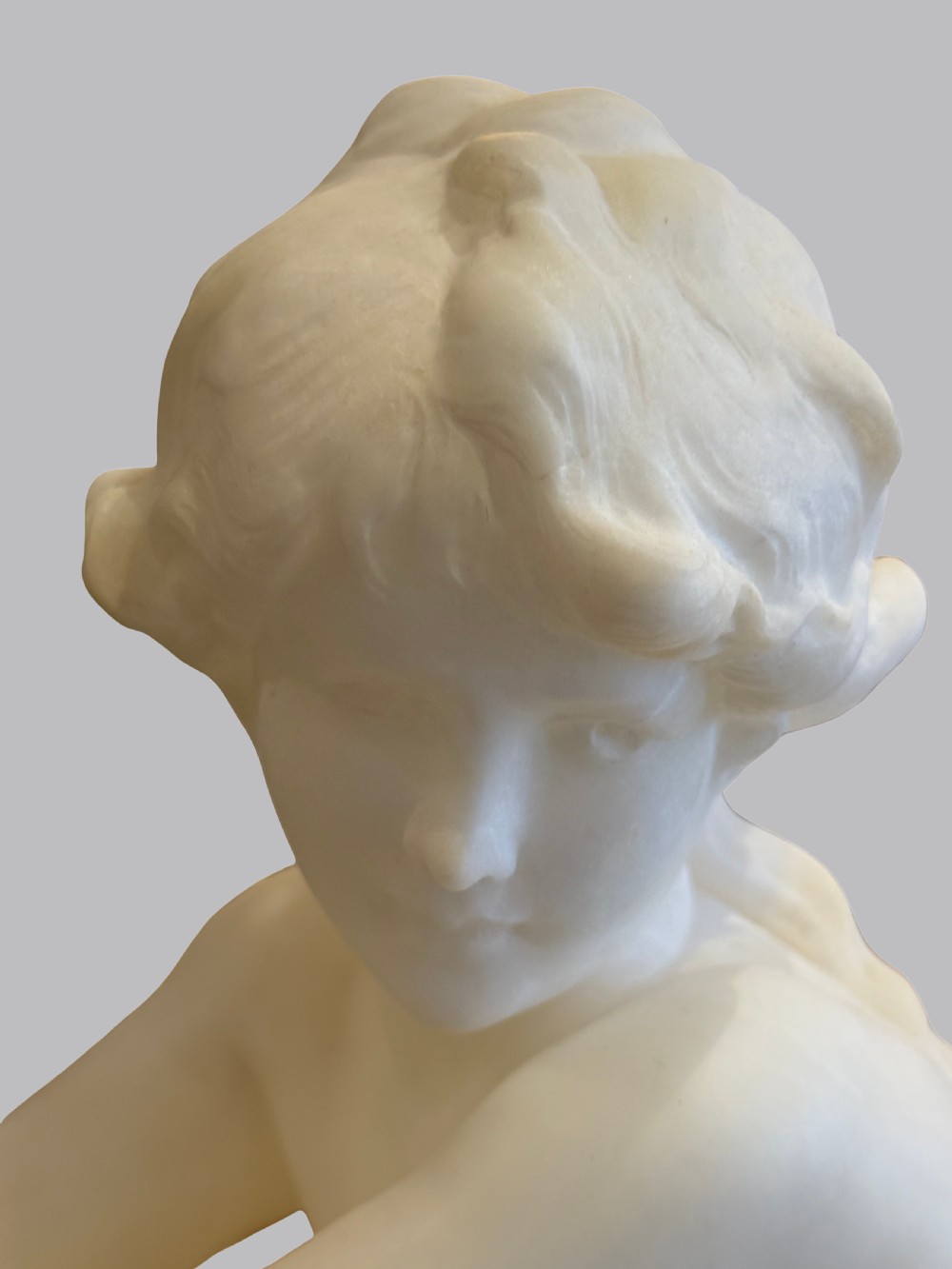 A carved off-white alabaster sculpture depicting a semi-clad reclining woman resting on a chaise longue set on a rectangular plinth. View III