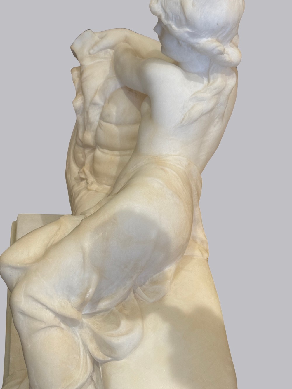 A carved off-white alabaster sculpture depicting a semi-clad reclining woman resting on a chaise longue set on a rectangular plinth. View IV