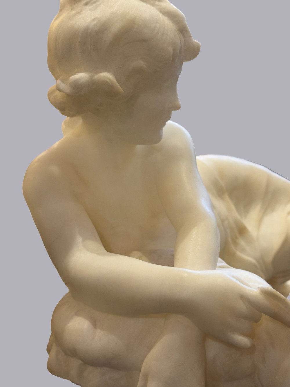 A carved off-white alabaster sculpture depicting a semi-clad reclining woman resting on a chaise longue set on a rectangular plinth. View V