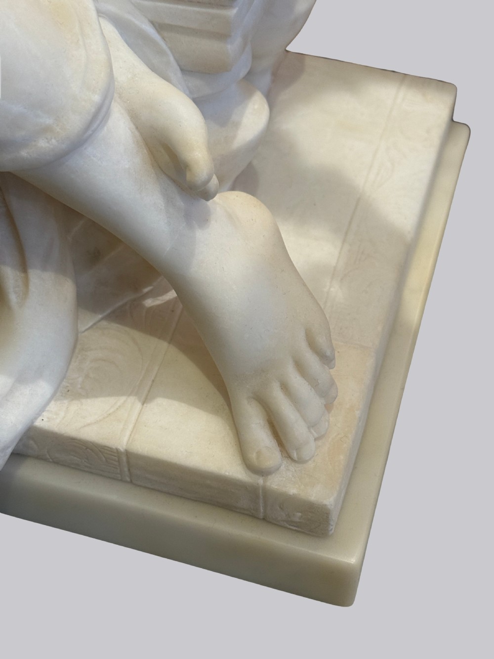 A carved off-white alabaster sculpture depicting a semi-clad reclining woman resting on a chaise longue set on a rectangular plinth. View VII