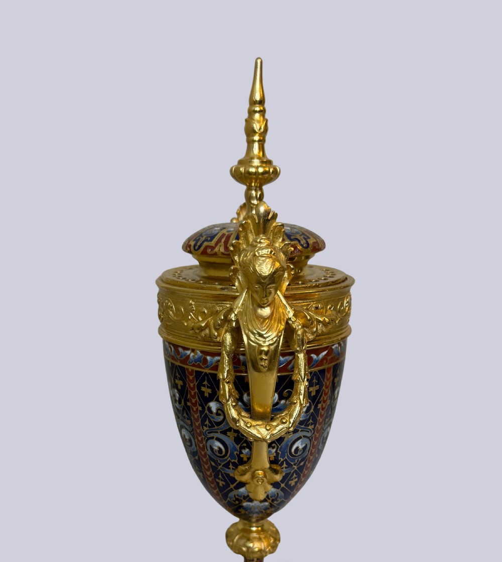 A 19th-century French lidded urn crafted from gilt bronze featuring blue and red champleve enamel detailing with figural handles and a finial lid. View II