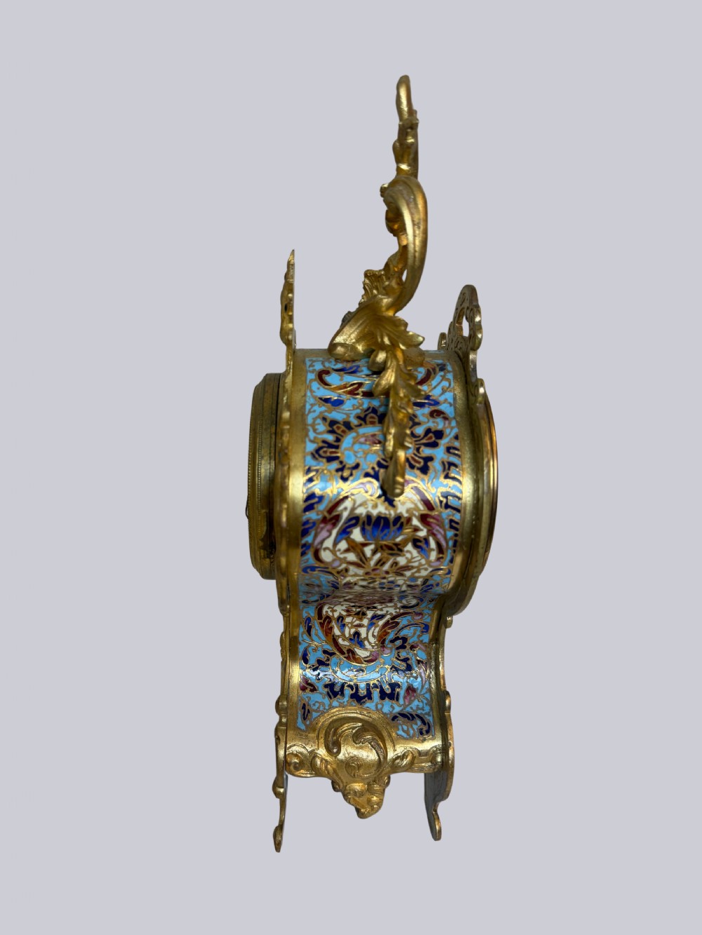 An ornate French Rococo Revival mantel clock featuring gilt bronze scrollwork, light blue champleve enamel patterns, and a white enamel dial with floral decoration, shown with a winding key. View III