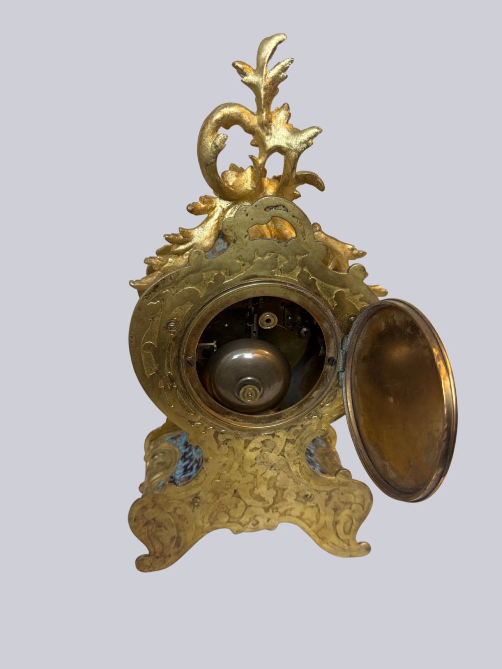 An ornate French Rococo Revival mantel clock featuring gilt bronze scrollwork, light blue champleve enamel patterns, and a white enamel dial with floral decoration, shown with a winding key. View V