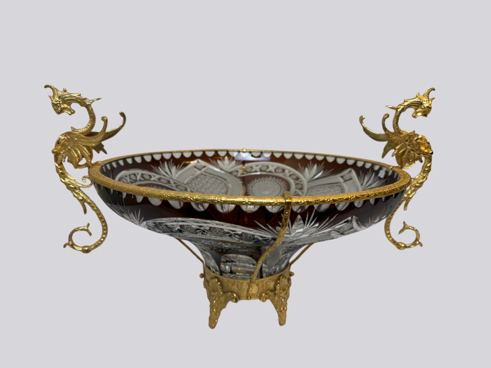 A deep red and clear cut glass bowl featuring gilt bronze dragon handles and a footed metal base.
