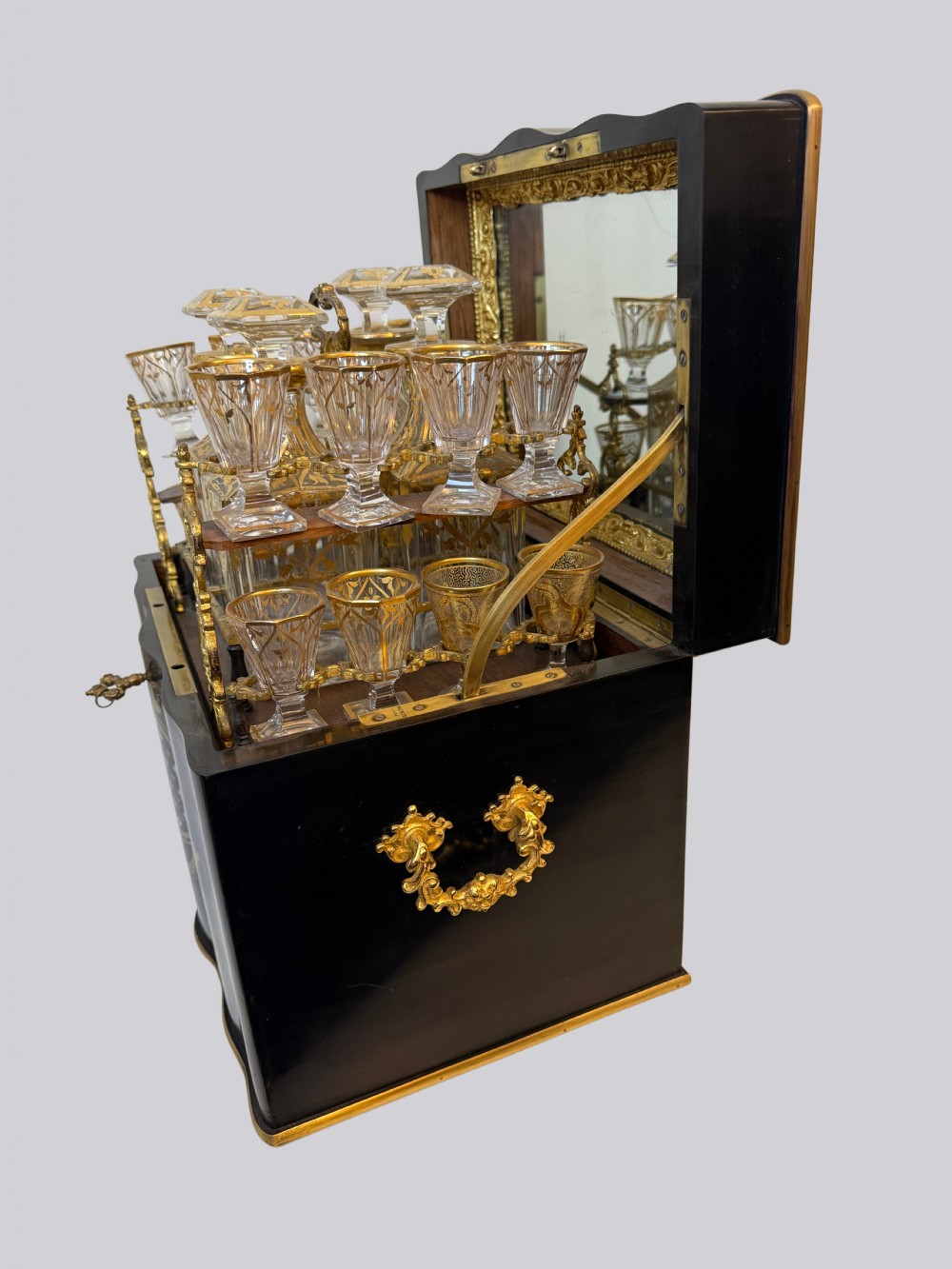 An open 19th-century ebonised wood cave a liqueur box featuring gilded crystal decanters and matching liqueur glasses on a tiered tray with ormolu mounts.