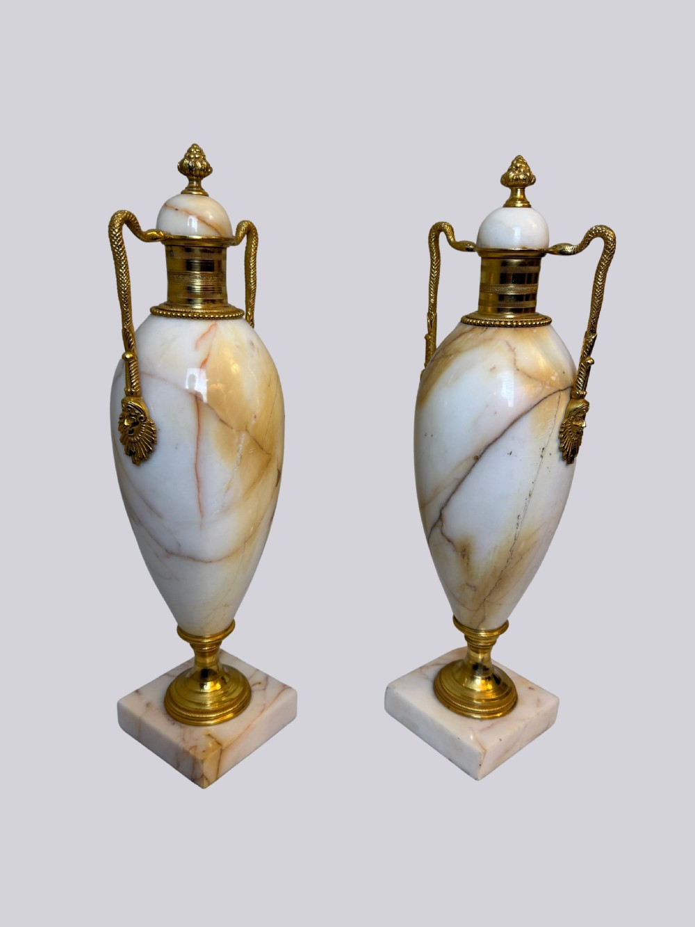 A pair of 19th-century ovoid white onyx urns featuring gilt bronze serpent handles, finials, and square pedestals. View II