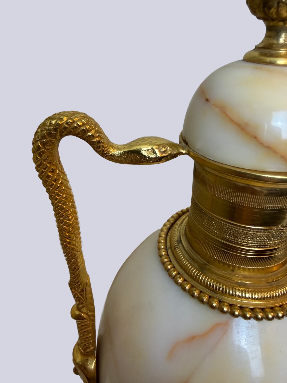 A pair of 19th-century ovoid white onyx urns featuring gilt bronze serpent handles, finials, and square pedestals. View IV