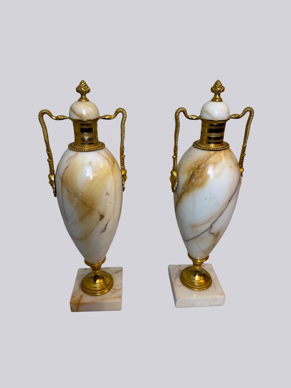 A pair of 19th-century ovoid white onyx urns featuring gilt bronze serpent handles, finials, and square pedestals. View VII