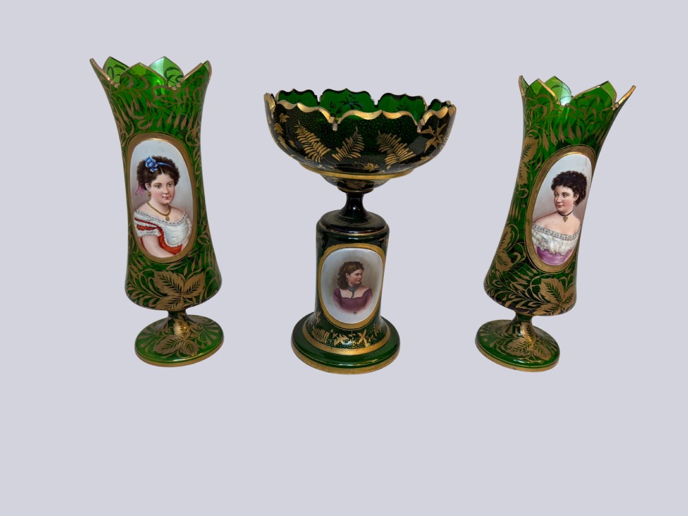 A three-piece emerald green Bohemian glass garniture set featuring gold gilt leaf patterns and oval enamel painted lady portraits.