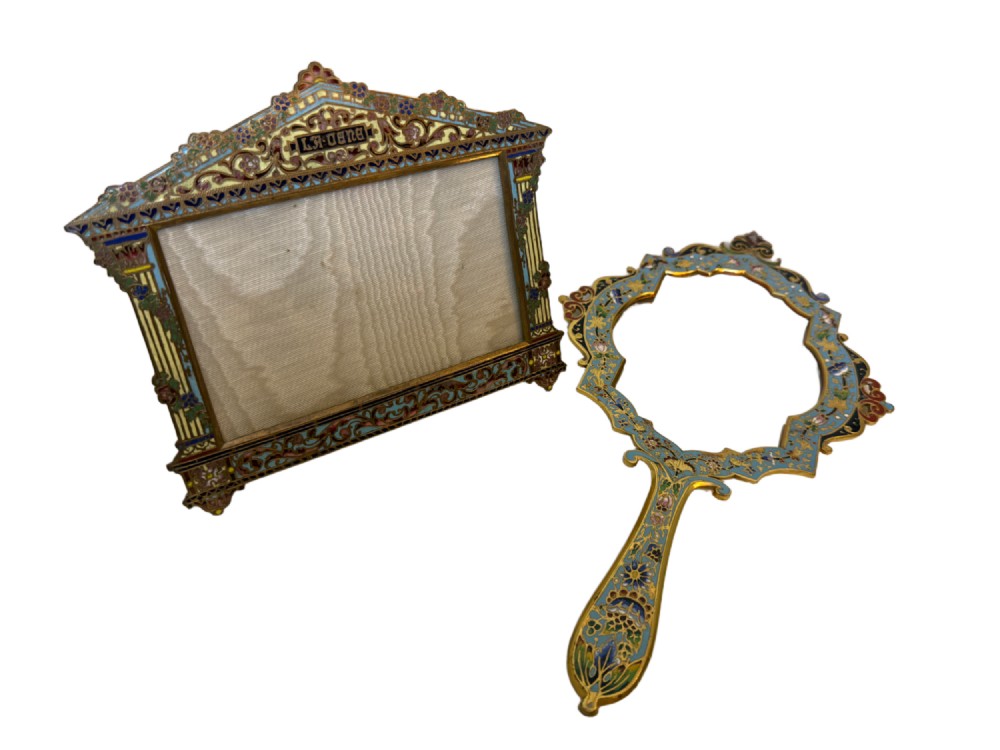 A 19th-century French gilt bronze and champleve enamel picture frame resting alongside a matching hand mirror with colourful floral motifs.