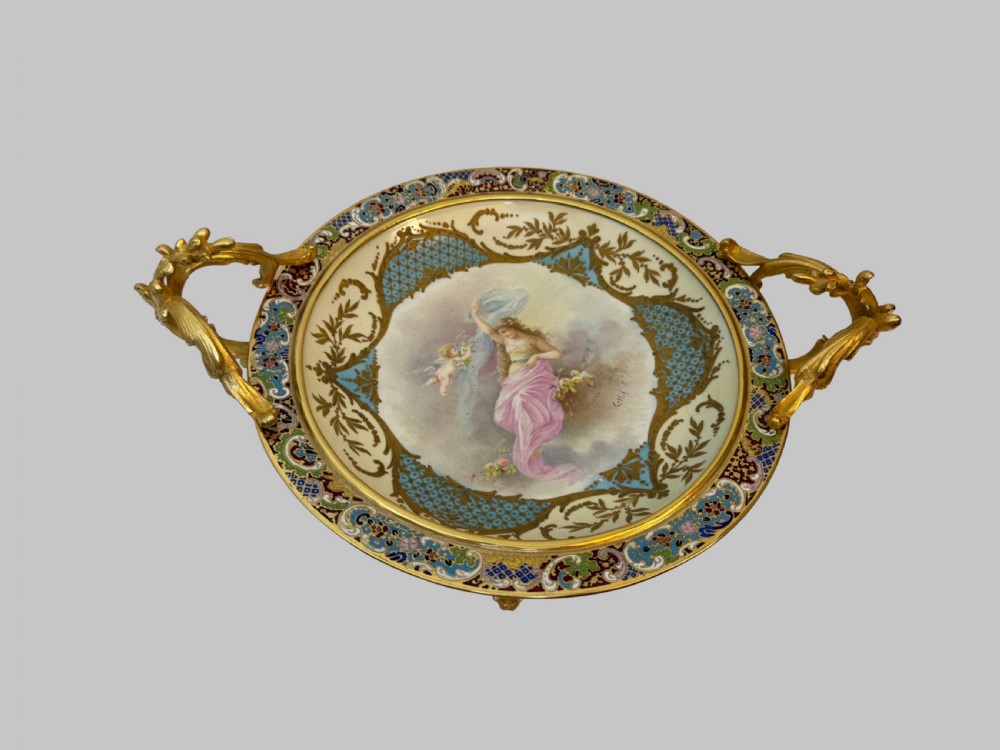 A circular 19th-century French porcelain centrepiece with hand-painted classical figures framed by colourful champleve enamel and twin gilt bronze handles.