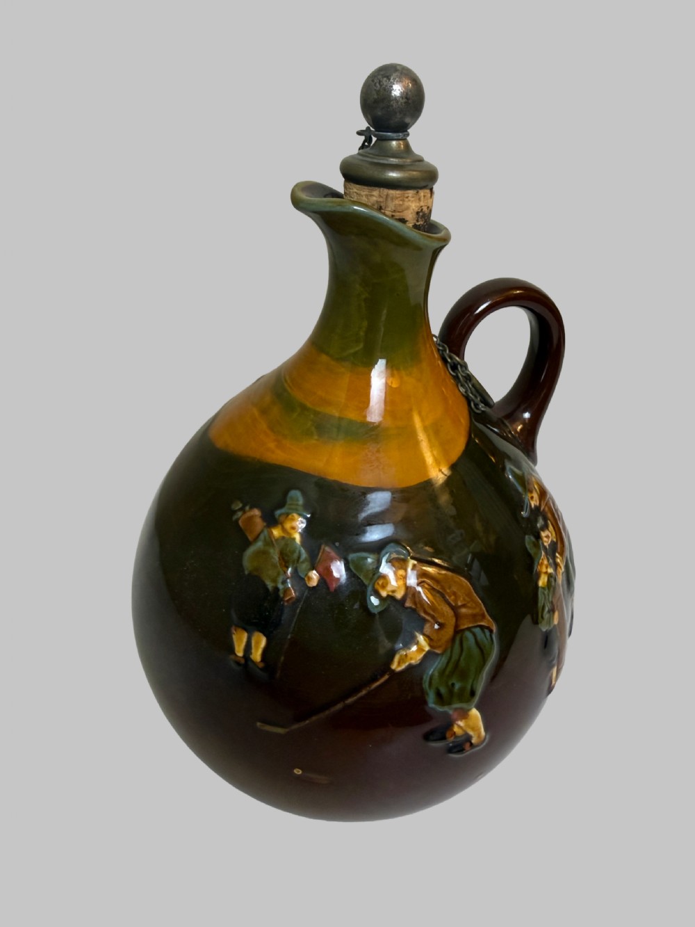 A brown and ochre glazed ceramic whisky flask featuring a raised relief figure of a golfer with an attached cork stopper on a metal chain. View II