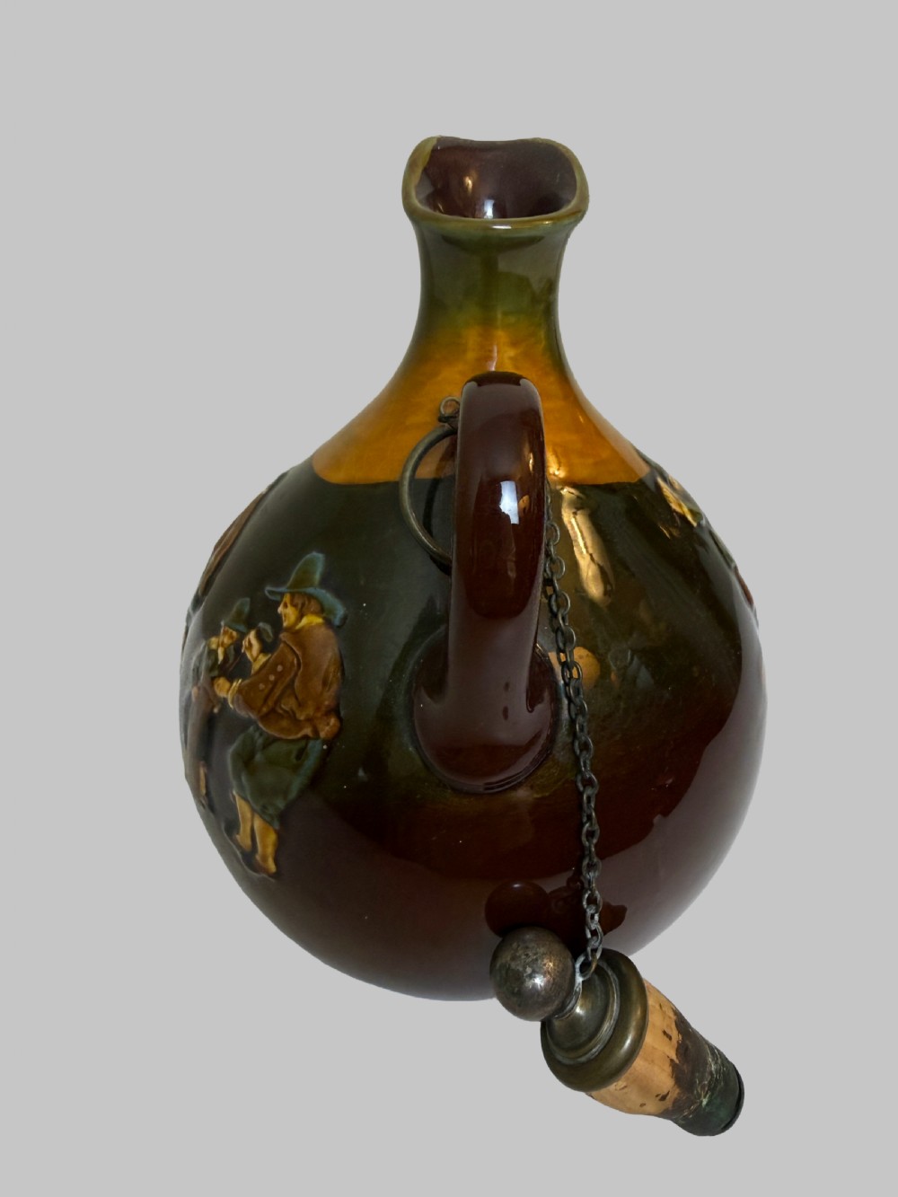 A brown and ochre glazed ceramic whisky flask featuring a raised relief figure of a golfer with an attached cork stopper on a metal chain. View VI