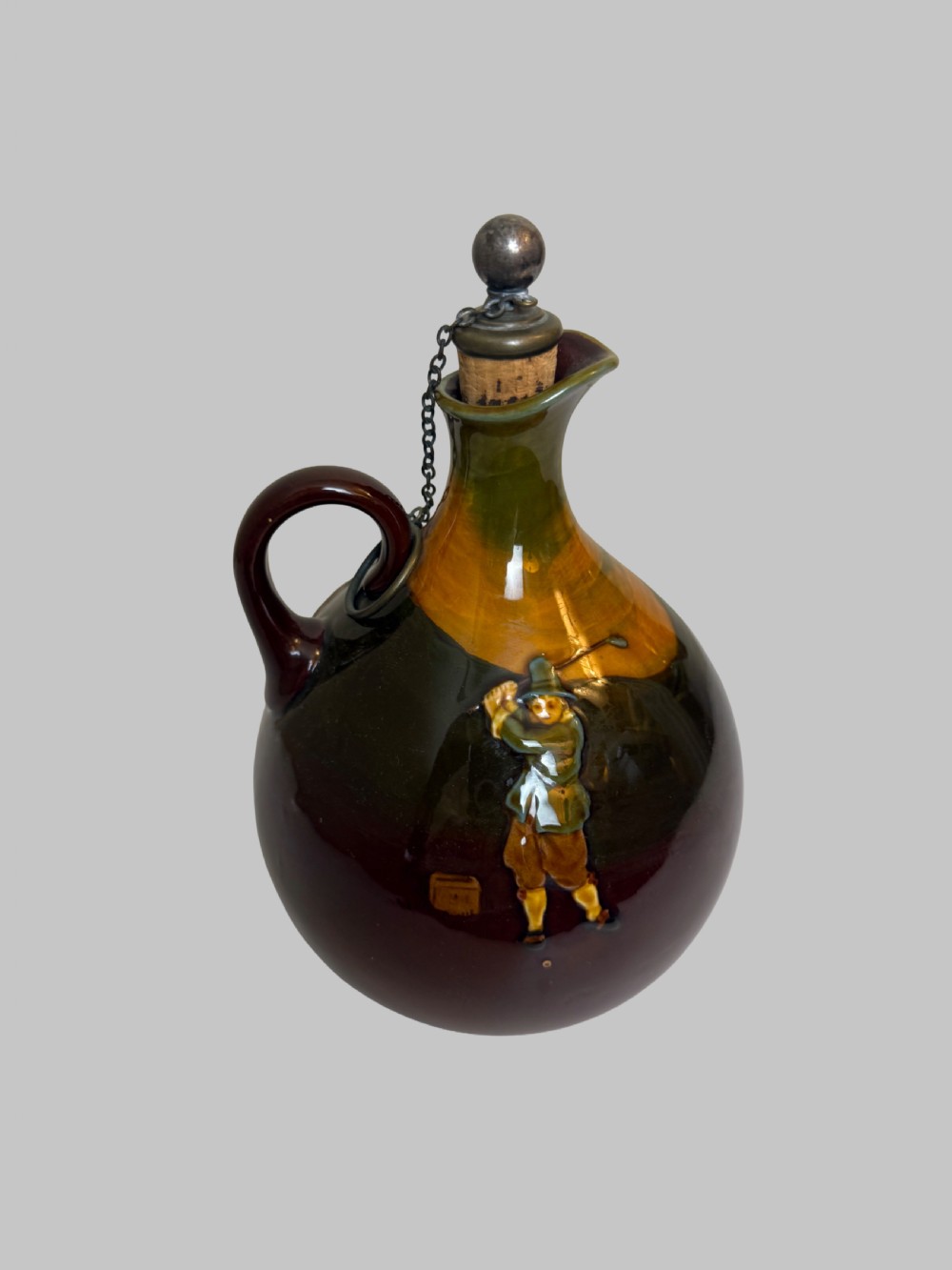A brown and ochre glazed ceramic whisky flask featuring a raised relief figure of a golfer with an attached cork stopper on a metal chain. View VII