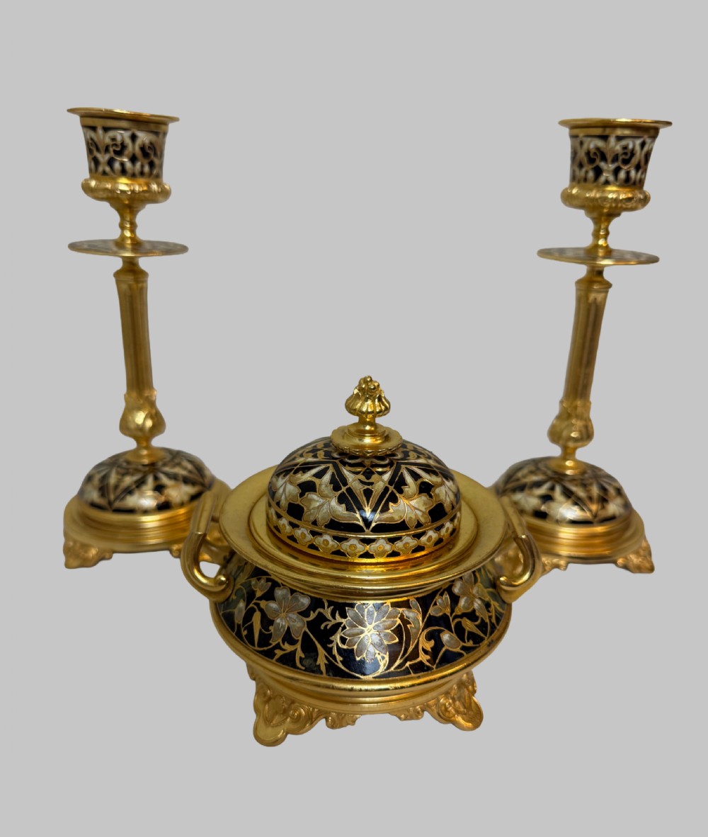 A nineteenth-century French writing set featuring a covered central inkwell flanked by two matching gilt bronze and champleve enamel candlesticks.