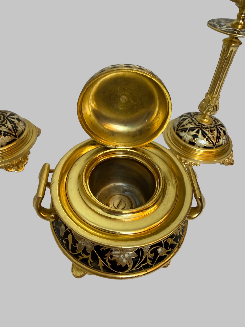 A nineteenth-century French writing set featuring a covered central inkwell flanked by two matching gilt bronze and champleve enamel candlesticks. View V