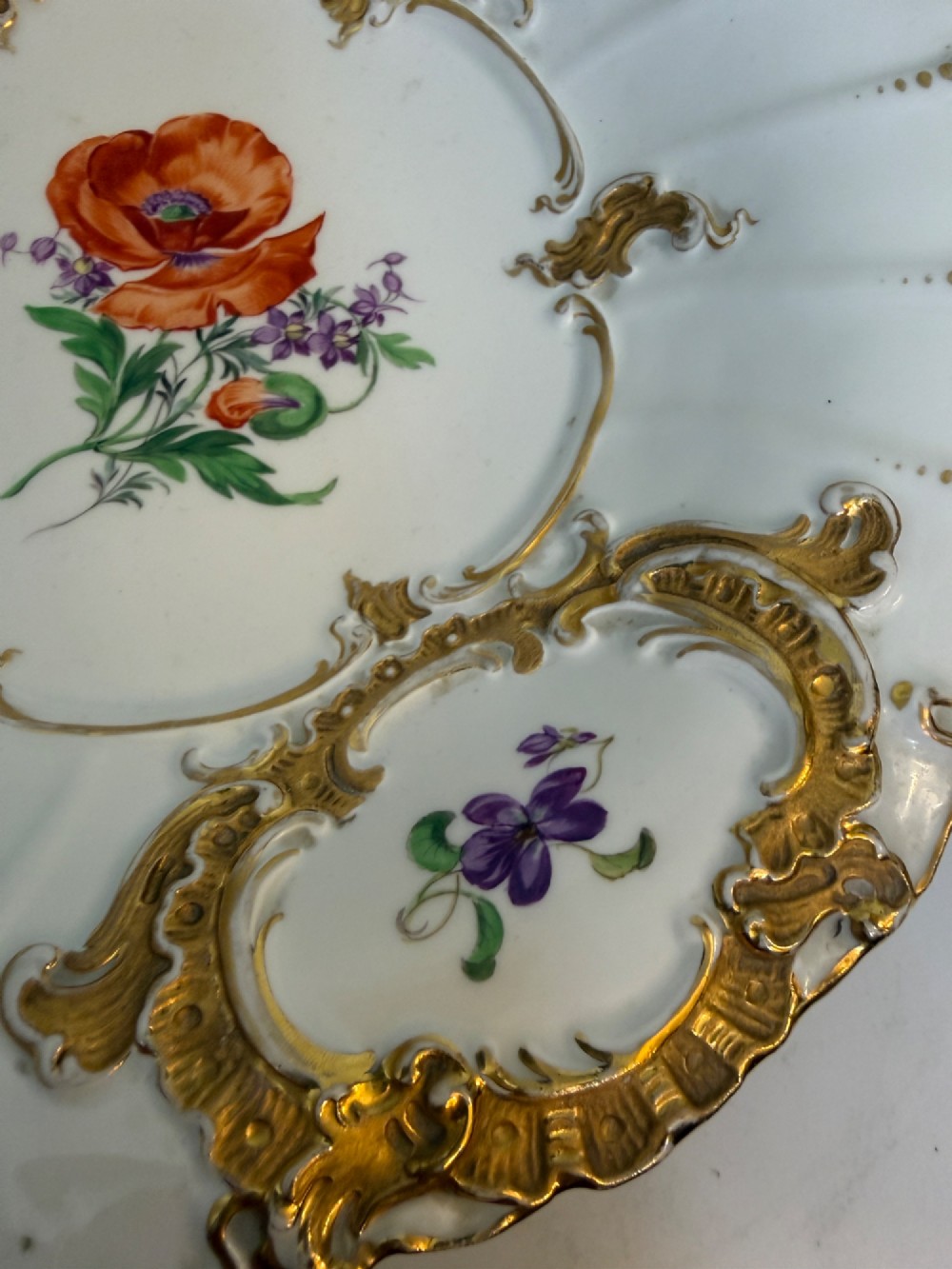 A white scalloped porcelain dish featuring hand-painted central botanical flowers surrounded by gilded Rococo cartouches containing smaller floral sprays. View III