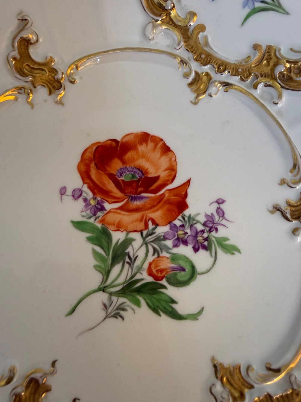 A white scalloped porcelain dish featuring hand-painted central botanical flowers surrounded by gilded Rococo cartouches containing smaller floral sprays. View IV