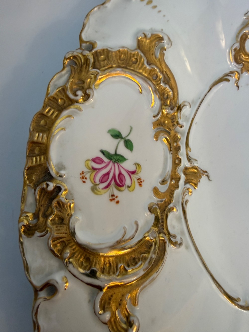 A white scalloped porcelain dish featuring hand-painted central botanical flowers surrounded by gilded Rococo cartouches containing smaller floral sprays. View V