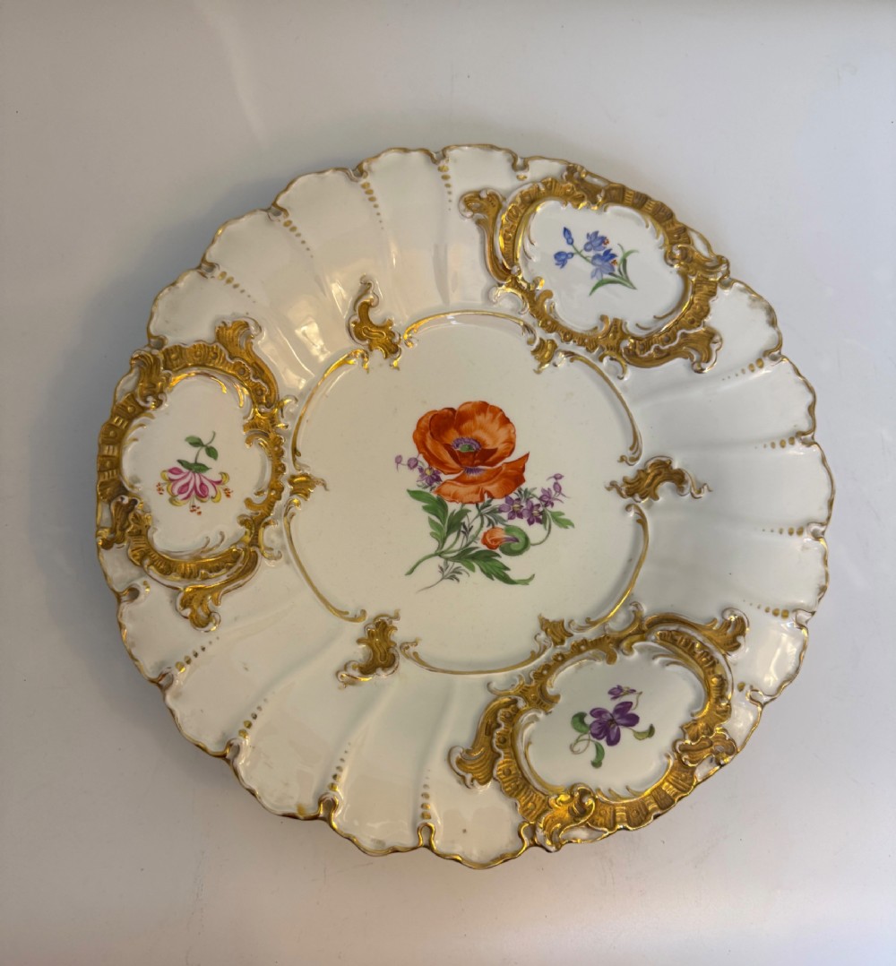 A white scalloped porcelain dish featuring hand-painted central botanical flowers surrounded by gilded Rococo cartouches containing smaller floral sprays. View VII