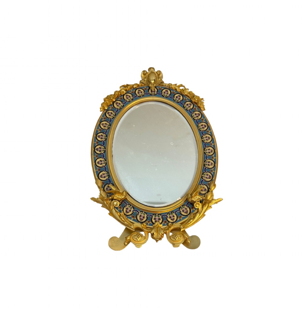 An oval late nineteenth-century French table mirror featuring a gilt bronze frame with blue champleve enamel scrollwork and ornate cast feet.