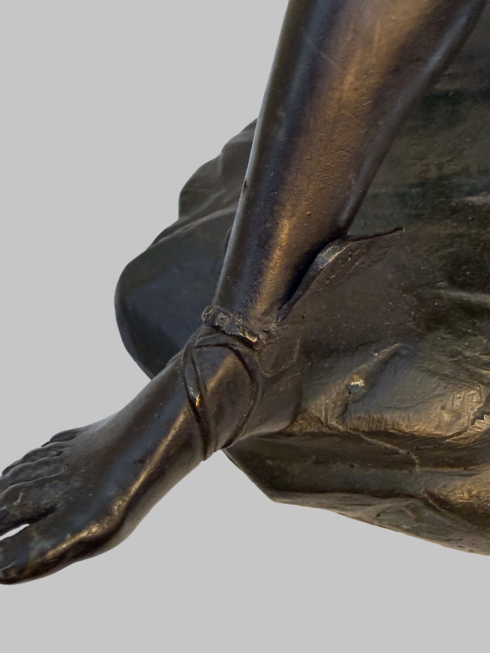 A dark patinated bronze sculpture depicting a classical male nude youth resting seated upon a rugged stone formation. View VI