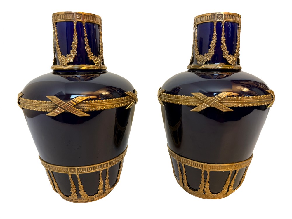 A pair of cobalt blue glass vases featuring ornate gilt bronze floral garlands, ribbon details, and metal rim mounts.