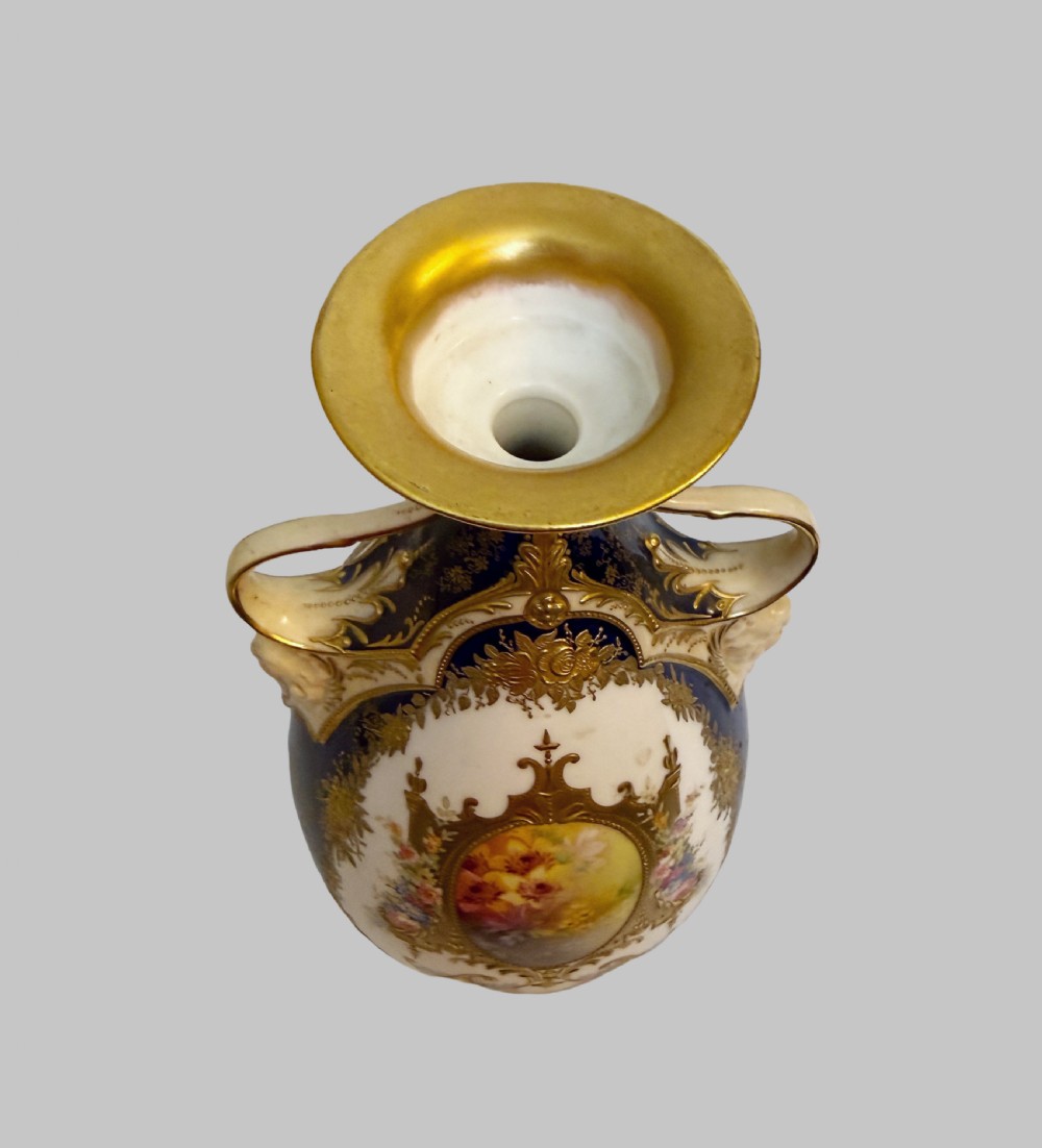An antique Royal Doulton porcelain vase featuring cobalt blue and white glazes, heavy gilt scrolling, scroll handles with mask terminals, and a central hand-painted floral panel. View V