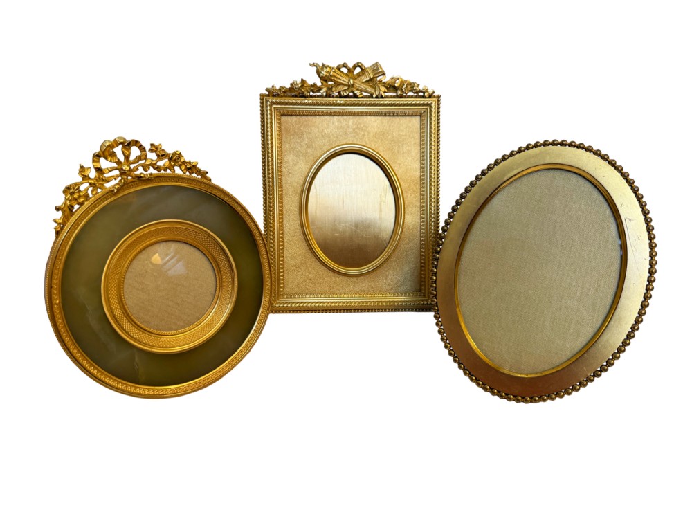 A trio of antique French gilt bronze picture frames featuring ribbon crests, beaded borders, and an onyx panel mount.