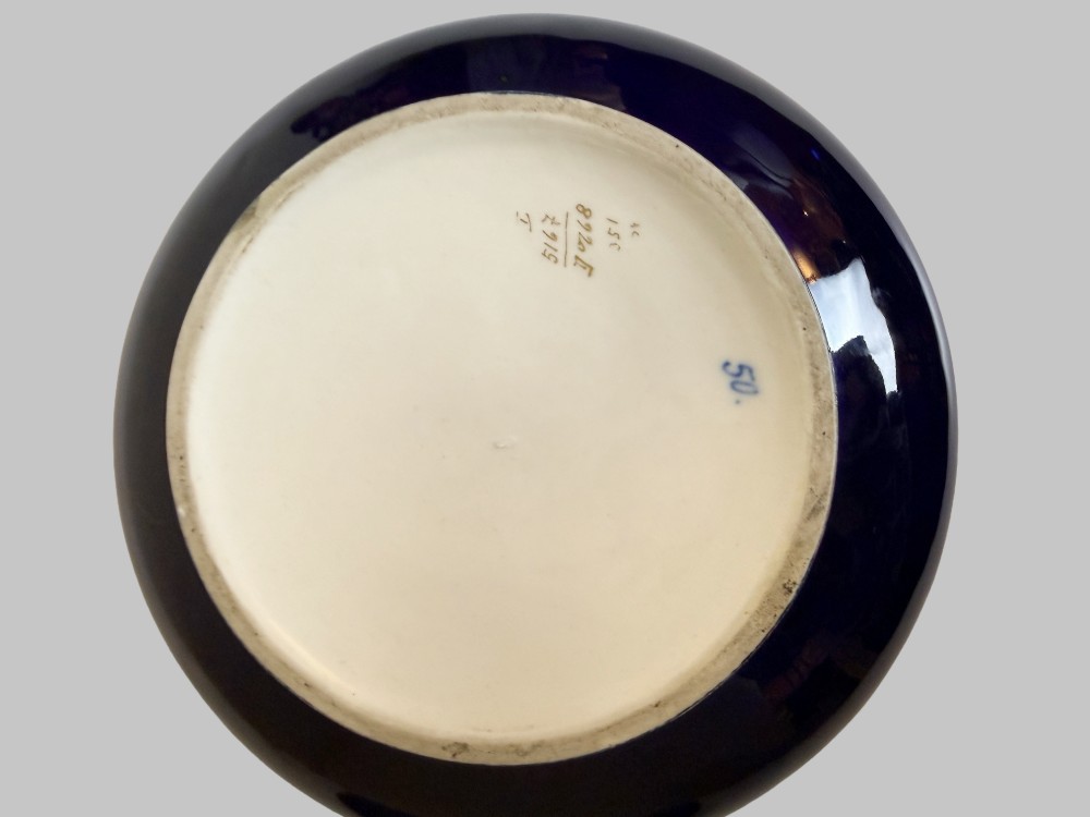 A circular antique French porcelain box featuring a central hand-painted classical scene of three women framed by cobalt blue, gilt embellishments, and white enamel dots. View VI