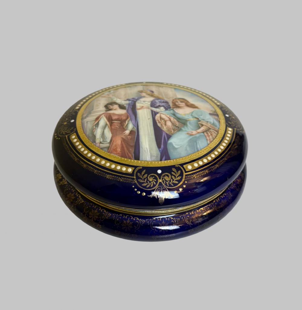 A circular antique French porcelain box featuring a central hand-painted classical scene of three women framed by cobalt blue, gilt embellishments, and white enamel dots. View VIII