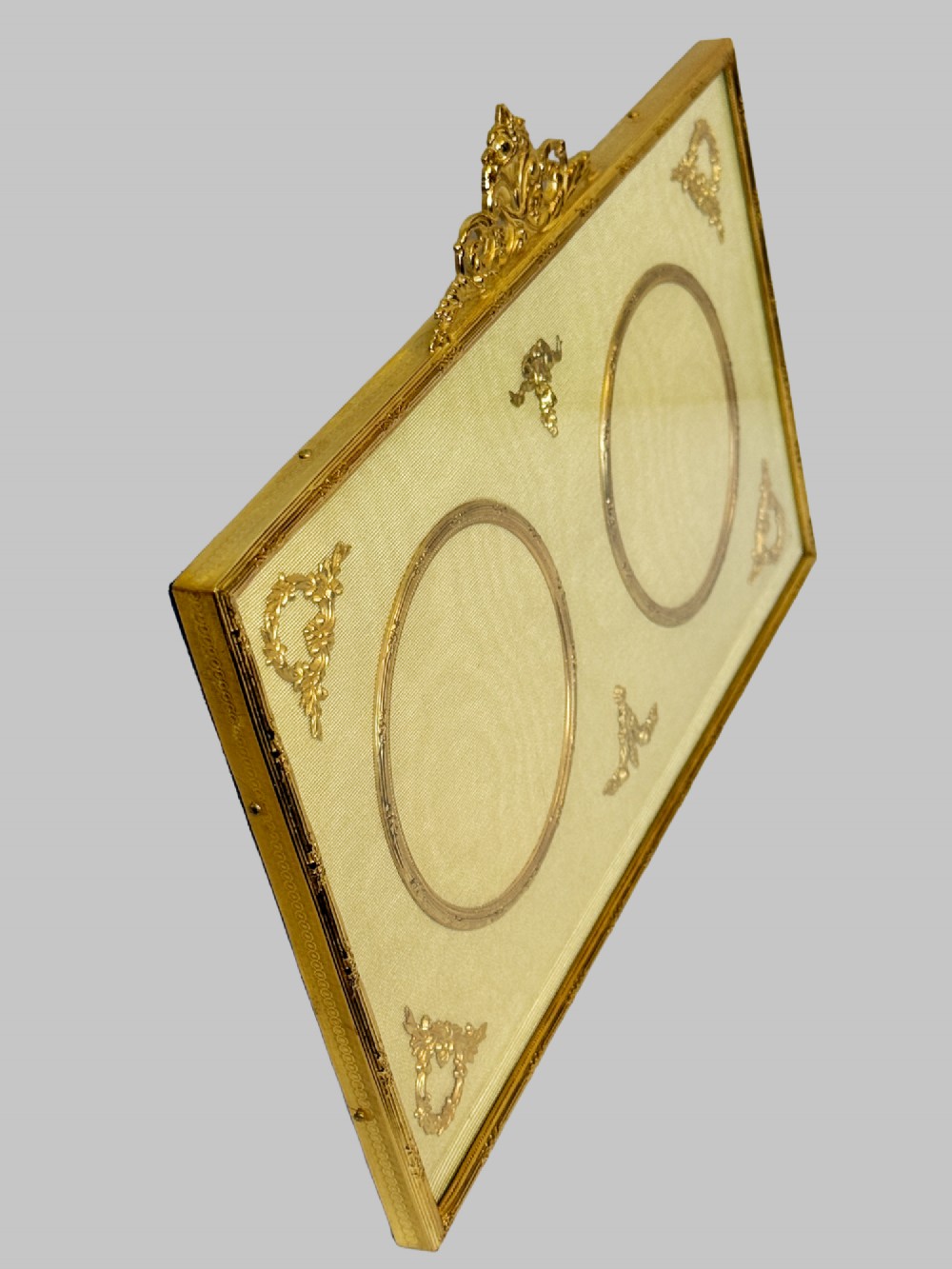 A 19th-century rectangular French gilt bronze frame featuring two circular photograph openings set against a cream silk background, adorned with a floral crest and ribbon mounts. View II