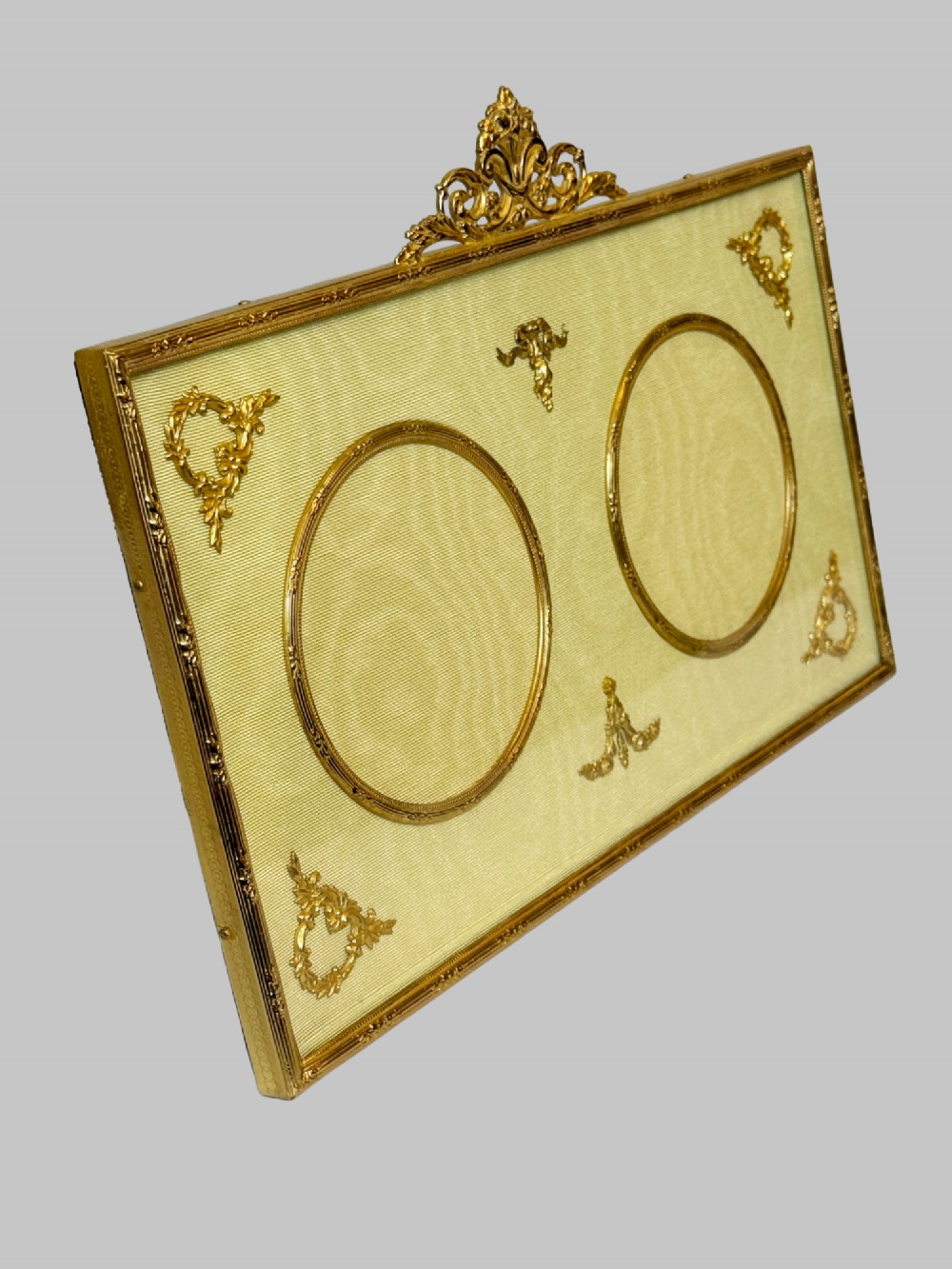 A 19th-century rectangular French gilt bronze frame featuring two circular photograph openings set against a cream silk background, adorned with a floral crest and ribbon mounts. View III