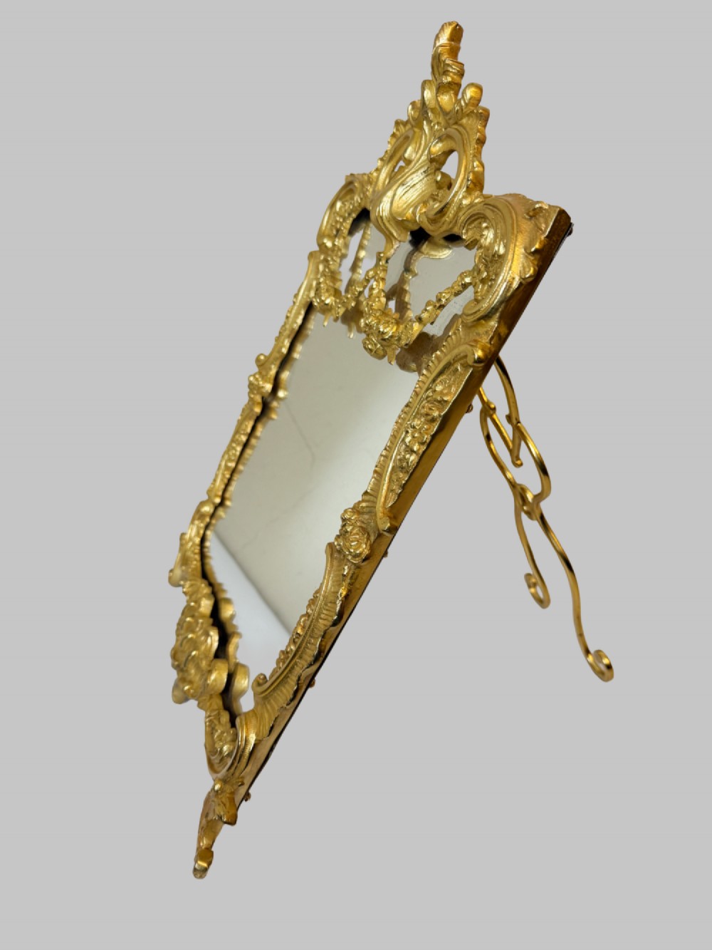An ornate gold gilt bronze table mirror featuring Rococo scrollwork, floral garlands, and a carved crest motif. View IV