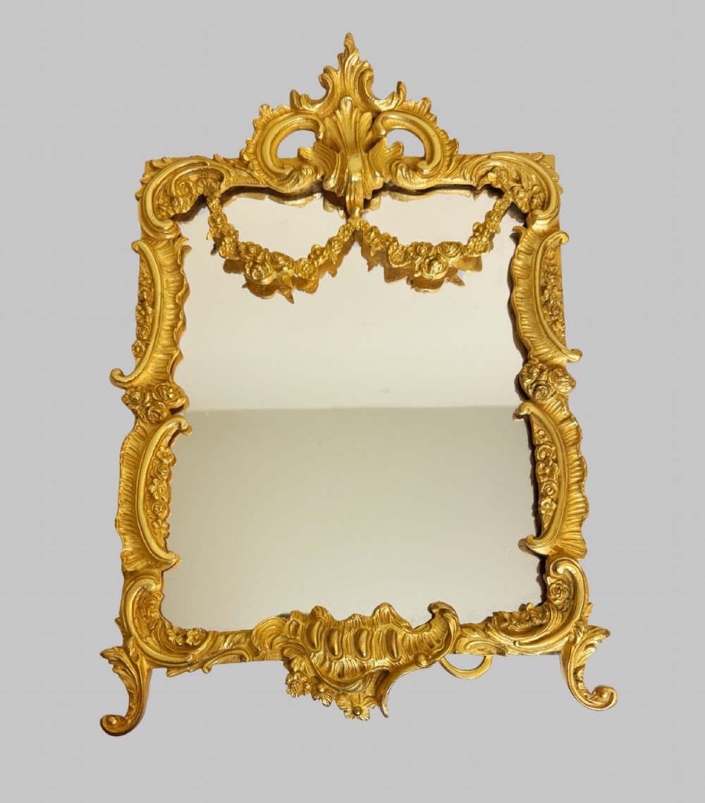 An ornate gold gilt bronze table mirror featuring Rococo scrollwork, floral garlands, and a carved crest motif. View IX