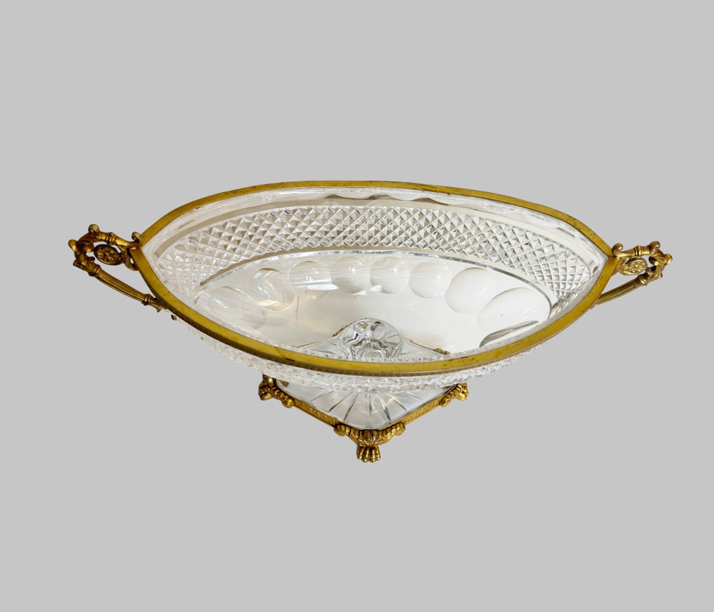 A late 19th-century French boat-shaped cut crystal centrepiece bowl set within gilded bronze mounts with dual scroll handles and a footed square base. View II