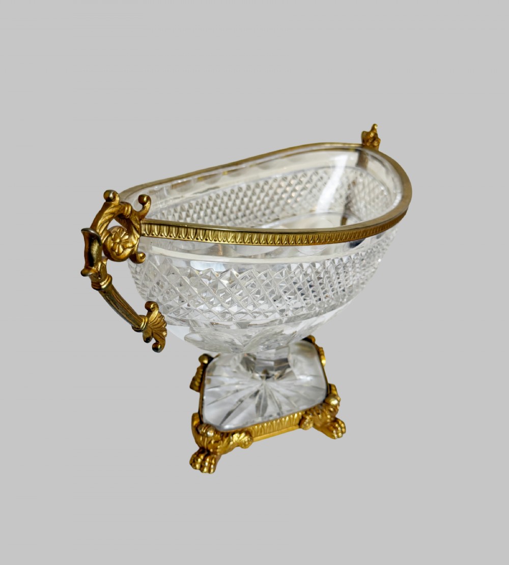 A late 19th-century French boat-shaped cut crystal centrepiece bowl set within gilded bronze mounts with dual scroll handles and a footed square base. View VIII