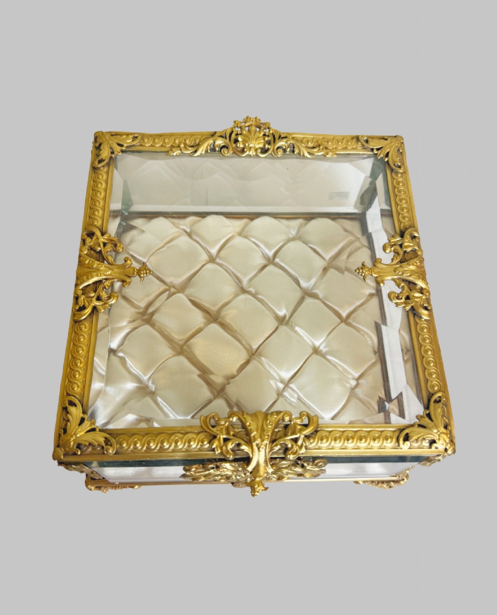 An antique rectangular bevelled crystal glass jewellery box featuring an ornate gilt bronze frame with decorative corner mounts and a button-tufted silk cushion interior. View II