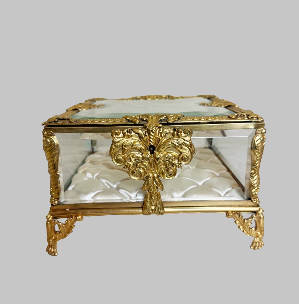 An antique rectangular bevelled crystal glass jewellery box featuring an ornate gilt bronze frame with decorative corner mounts and a button-tufted silk cushion interior. View III