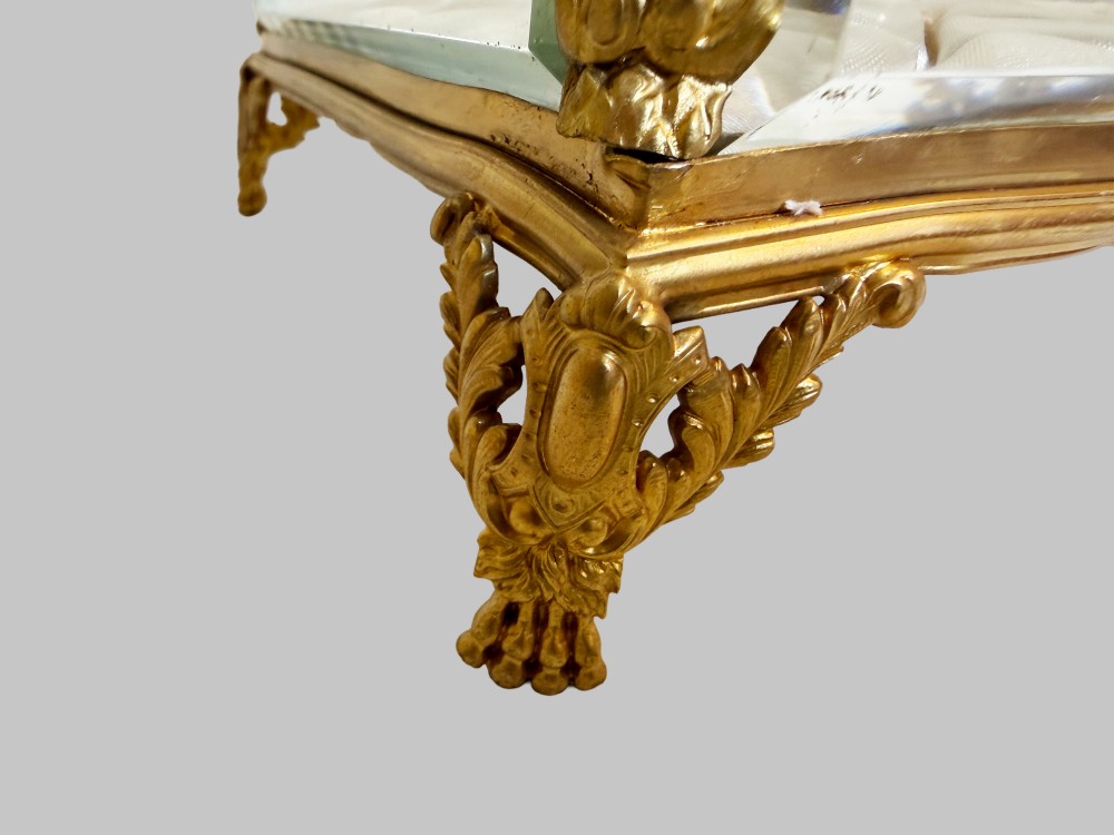 An antique rectangular bevelled crystal glass jewellery box featuring an ornate gilt bronze frame with decorative corner mounts and a button-tufted silk cushion interior. View VII