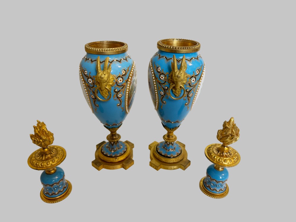 A pair of turquoise blue enamelled cassolette urns featuring gilt-bronze ram head handles, flame finials, and painted romantic pastoral vignettes. View VI