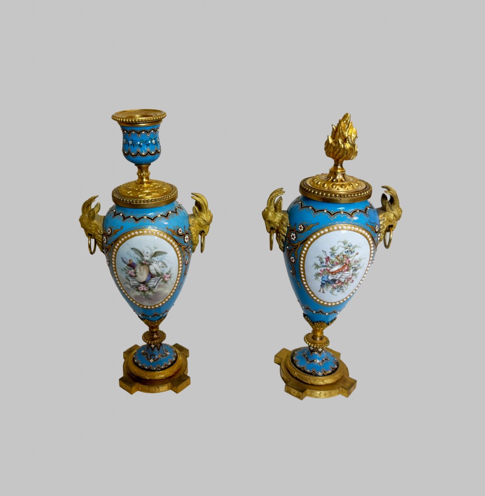 A pair of turquoise blue enamelled cassolette urns featuring gilt-bronze ram head handles, flame finials, and painted romantic pastoral vignettes. View X