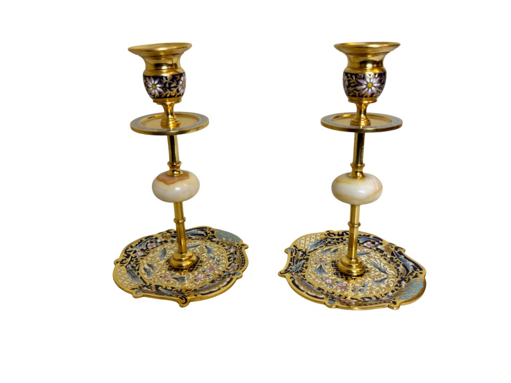 A pair of 19th-century gilt bronze candlesticks featuring floral champleve enamel decoration, central onyx knops, and shaped wide bases.