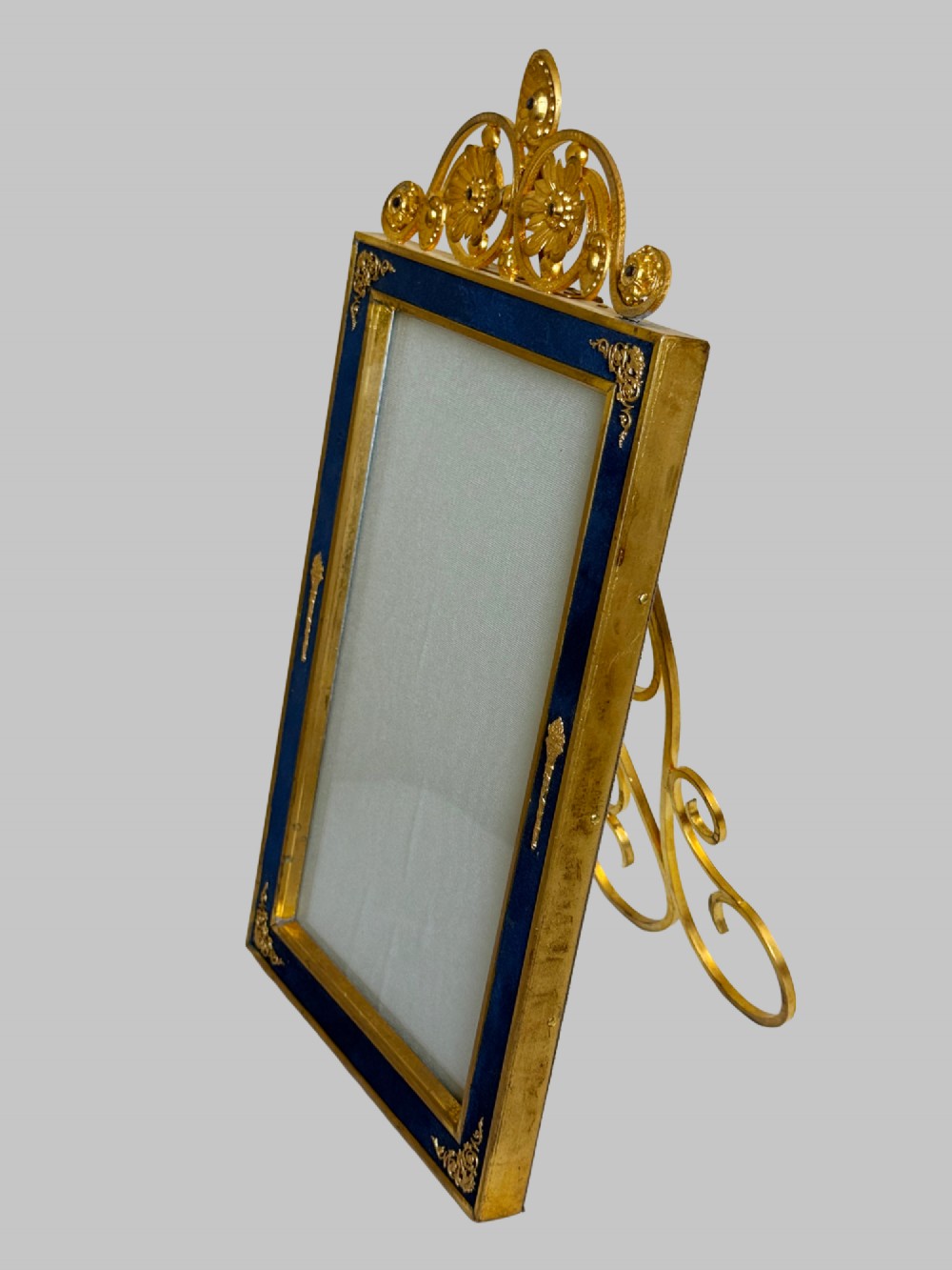 A rectangular gilt bronze picture frame featuring a blue velvet border, ornate corner mounts, and an elaborate floral crest at the top. View II