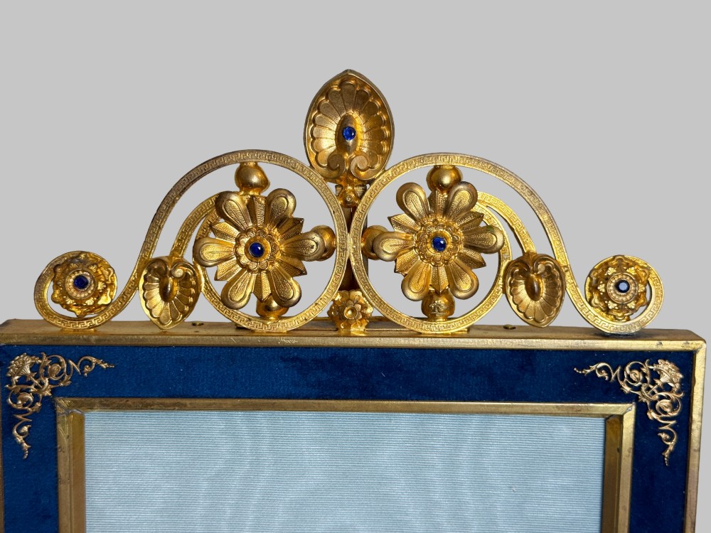A rectangular gilt bronze picture frame featuring a blue velvet border, ornate corner mounts, and an elaborate floral crest at the top. View VI